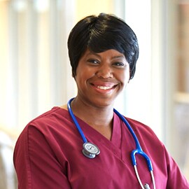 Smiling nurse in burgundy scrubs wearing a 3M Littmann Classic III Stethoscope with blue tubing.
